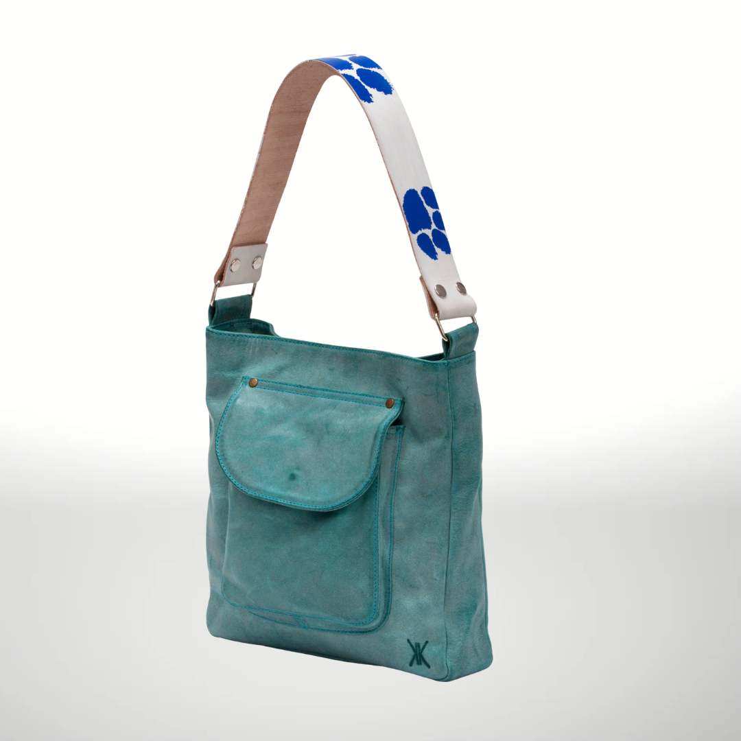 Turquoise shoulder bag with a white strap featuring blue paw prints on a light gray background